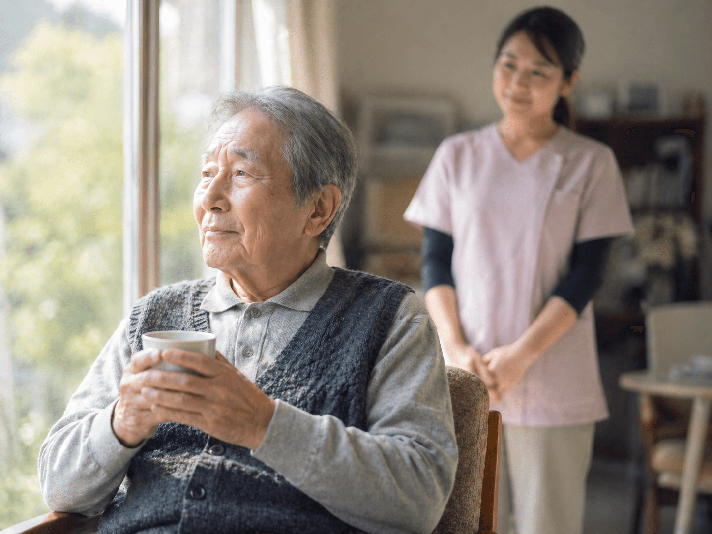 窓辺で穏やかに過ごす利用者と、優しく見守る介護スタッフ